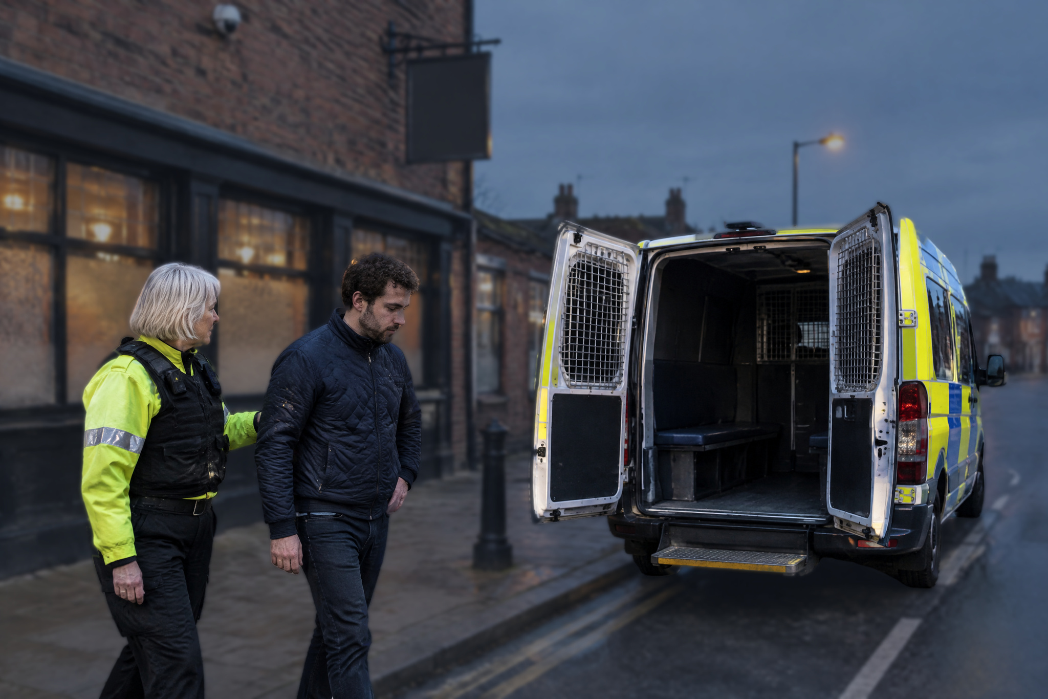 Officer leading a man to a police van outside a pub after violent disorder