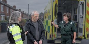Police officer holding a man beside a paramedic after alleged assault offences