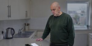 Man standing looking at a phone and letter after domestic abuse charges